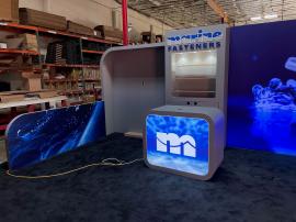 Custom Inline Exhibit with Backlit Fabric Graphics, Backlit Logo, Large Monitor Mount, Puck Lights, Backwall Locking Storage, (3) Shelves, MOD-1573 Counter, Product Display, and Corral Walls with Graphics